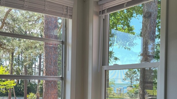 A room with a dark green sofa, a window with a view of trees and a lawn, and a chair by the window.