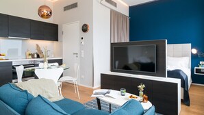 A modern living room with a sofa, a flat-screen TV, a dining table, and a kitchen area with cabinets and a stove. - Vienna Residence, Philips Haus - Euro Plaza #6589 (Vienna)