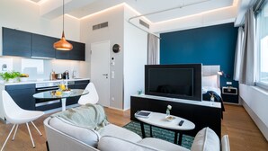 A modern living room with a sofa, a coffee table, a TV, and a kitchen area with cabinets and a dining table. - Vienna Residence, Philips Haus - Euro Plaza #6605 (Vienna)