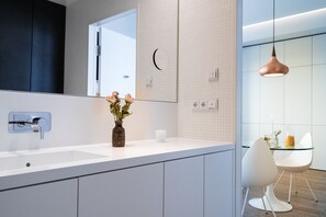 Une cuisine moderne avec un plan de travail blanc, un vase rempli de fleurs, une machine à café et une table en verre avec des chaises.