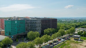 Ein mehrstöckiges Hotel mit grüner Fassade, umgeben von Bäumen und parkenden Autos.