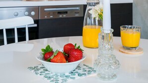 A modern kitchen with dark cabinets, a white countertop, a coffee maker, a kettle, a candle, a bowl of strawberries, and two glasses of orange juice.