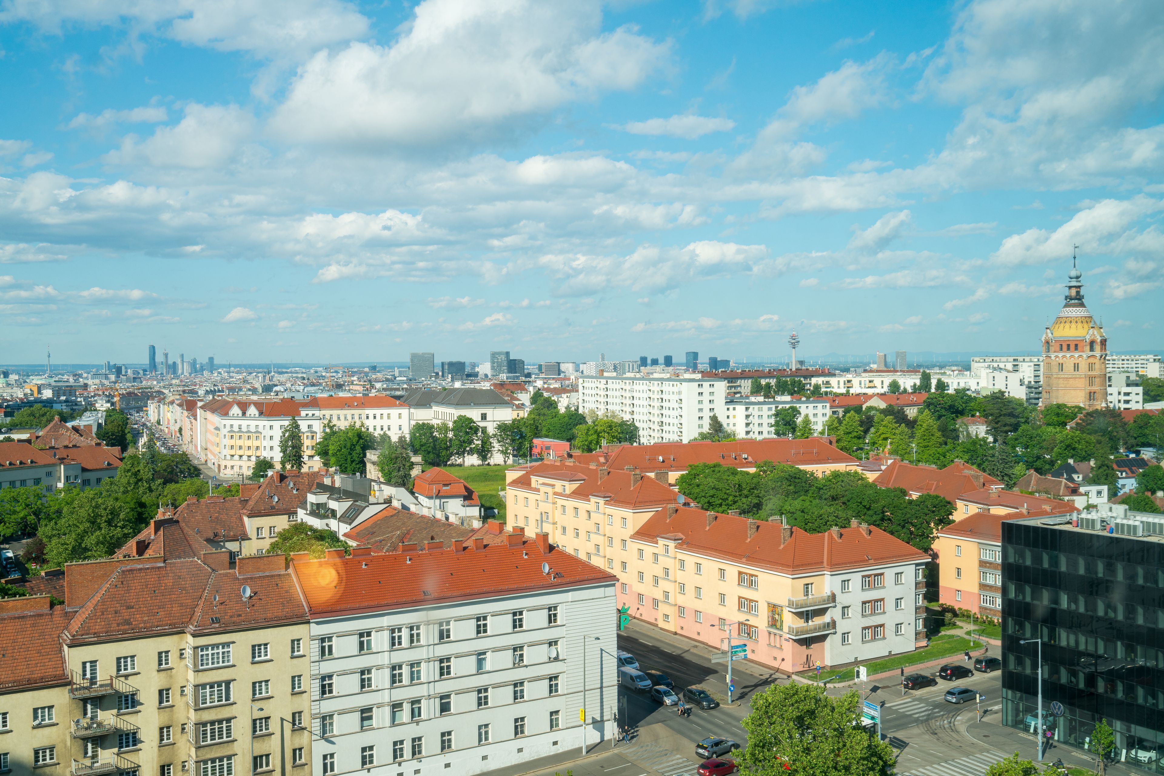 Eine Stadtansicht mit einer Mischung aus historischen und modernen Gebäuden, einem markanten Turm und wolkenlosem Himmel.