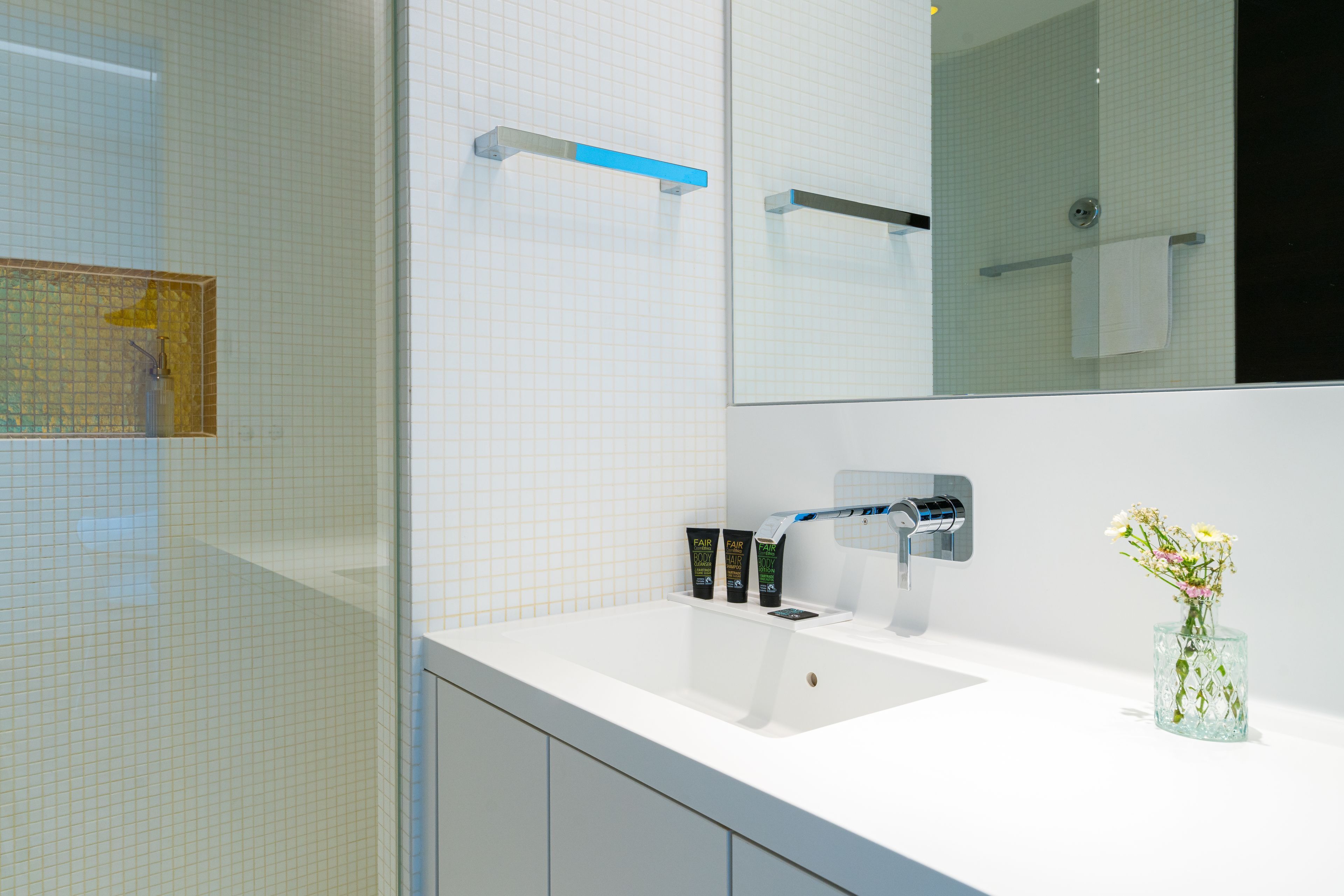 A modern bathroom with a white sink, a mirror, and a glass vase with flowers.