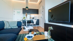 Un salon moderne avec un canapé, une table basse sur laquelle se trouve un saladier rempli de myrtilles, et un téléviseur fixé au mur.