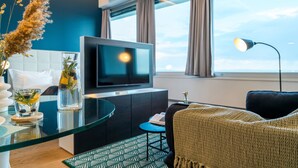Un salon moderne avec une table basse en verre, un téléviseur à écran plat, un canapé et une vue sur le ciel grâce à de grandes fenêtres.