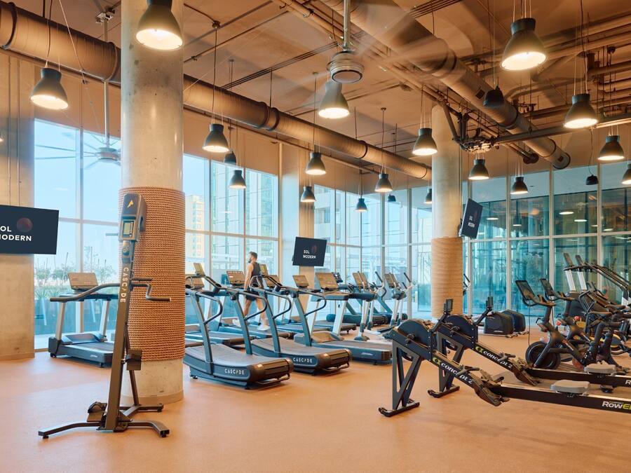 A gym with treadmills, rowing machines, and exercise bikes, large windows, and a modern industrial design.