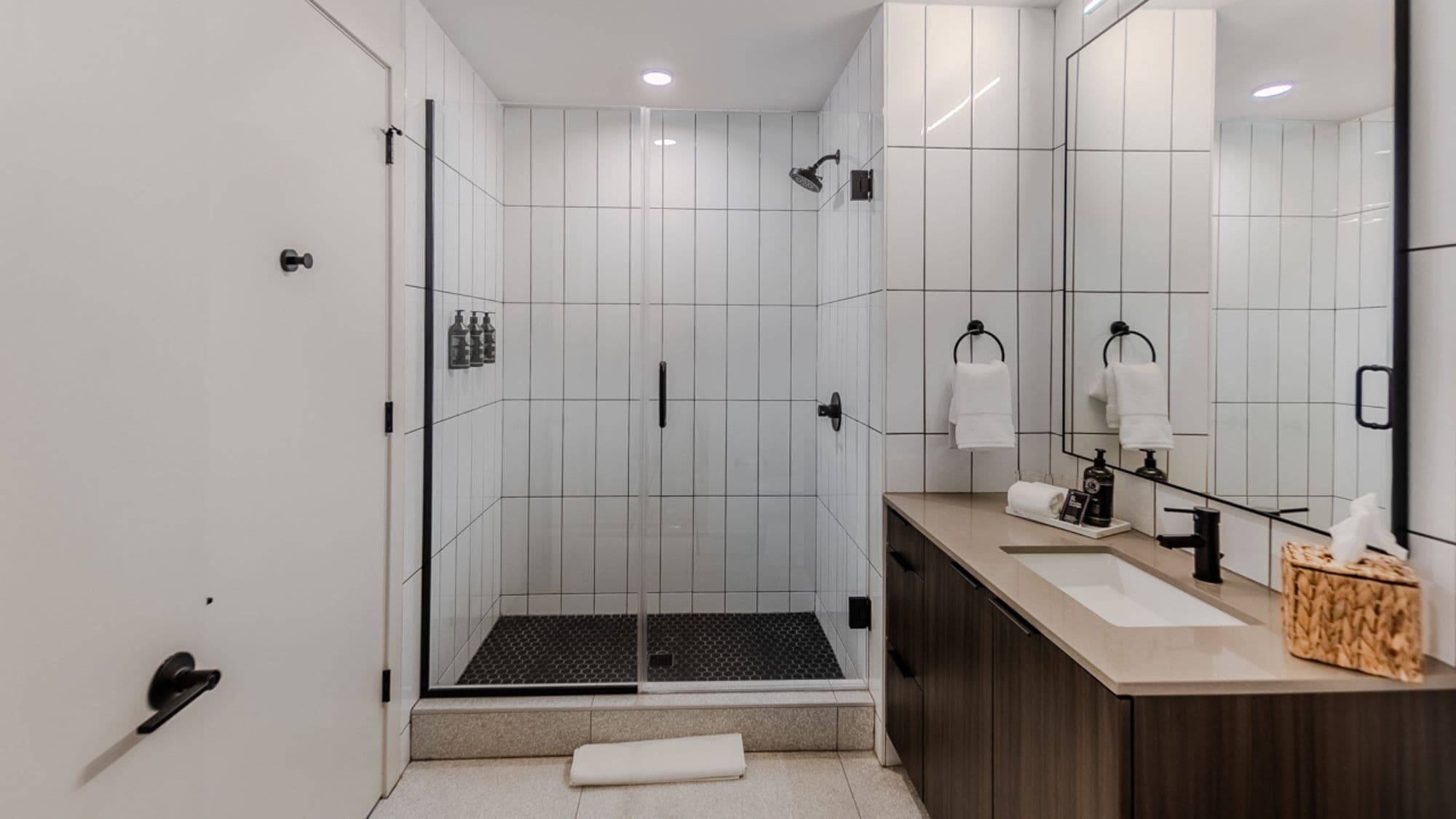 A modern bathroom with a glass-enclosed shower, a vanity with a mirror, and a towel rack.