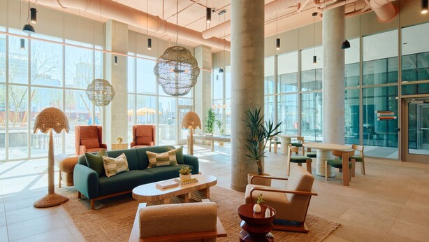 A spacious lobby with large windows, a green sofa, a round coffee table, and a large pillar. - Sentral Sol Modern (Phoenix)
