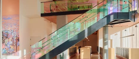 Un interior moderno con una escalera de cristal, un cuadro abstracto grande y una zona de recepción.