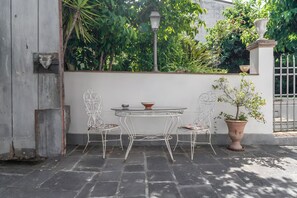 A patio with a metal table and chairs, a potted plant, and a wall-mounted light fixture. - Apartment 'Fatima' with Private Garden and Wi-Fi (Lucca)