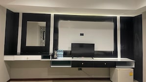 A modern room with a flat-screen TV, a small refrigerator, and a mirror above a counter. - hotel lucky palace  (Bangkok)