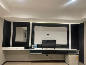 A modern room with a flat-screen TV, a small refrigerator, and a mirror above a counter. - hotel lucky palace  (Bangkok)