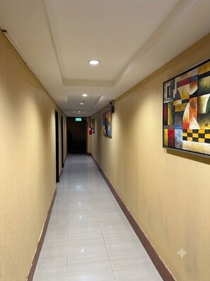 Un couloir d’hôtel avec un sol à motifs à carreaux, un éclairage encastré et une œuvre d’art accrochée au mur.