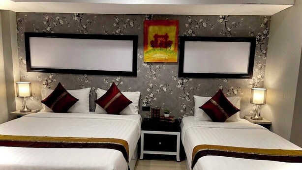 A hotel room with two beds, a nightstand between them, and a floral wallpaper. - hotel lucky palace  (Bangkok)