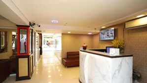 A hotel reception area with a marble counter, a television mounted on the wall, and a seating area with a sofa. - hotel lucky palace  (Bangkok)