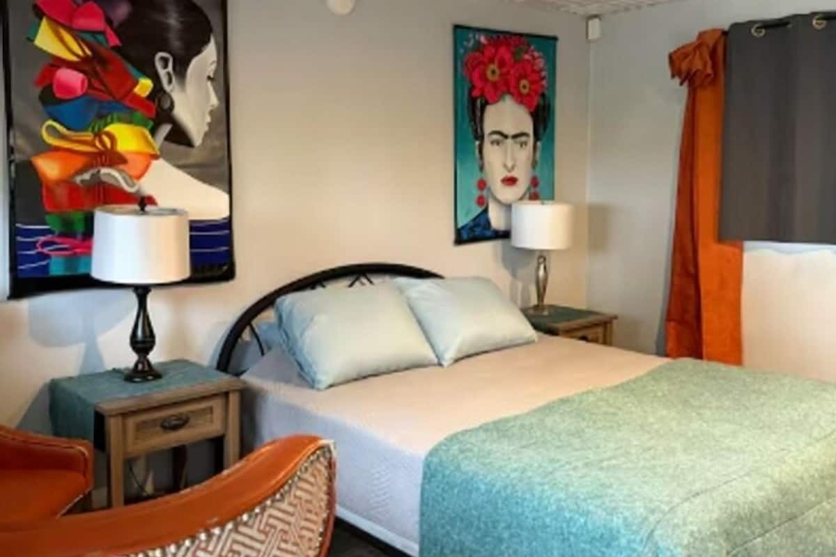 A hotel room with a bed, two bedside tables, a chair, and two paintings on the walls.