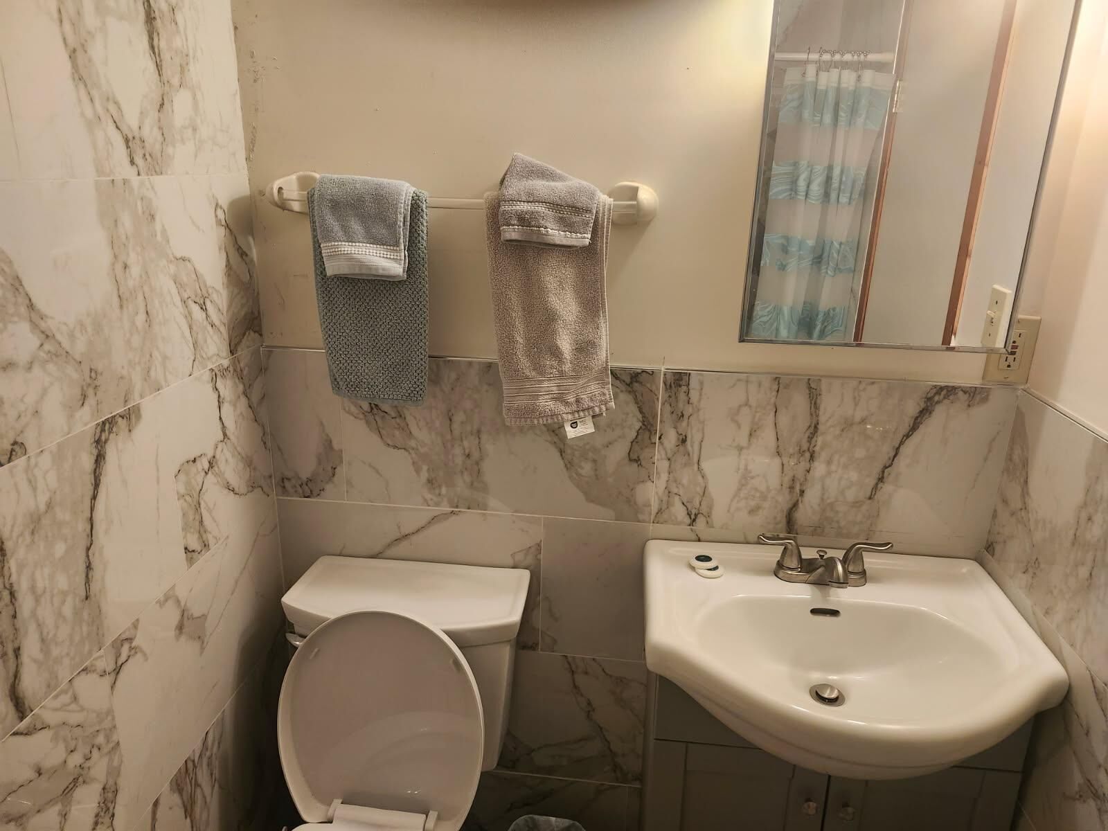 A bathroom with a toilet, sink, and marble walls.