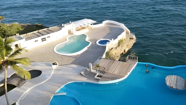 Ein Resort mit einem großen Infinity-Pool, einem kleineren Pool und einer Holzterrasse mit Blick aufs Meer.