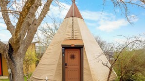 A conical tent with a brown door, surrounded by trees and a stone pathway. - Tipis on the Guadalupe (New Braunfels)