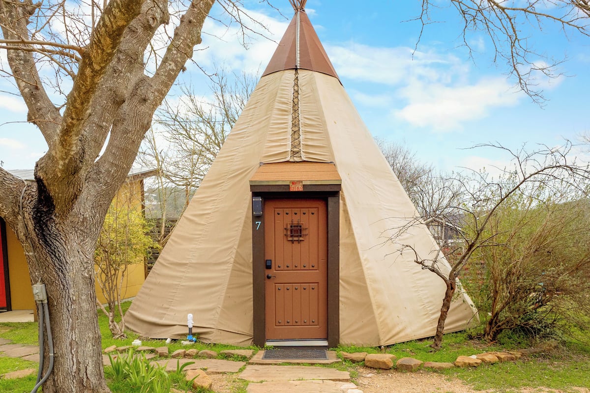 A conical tent with a brown door, surrounded by trees and a stone pathway.