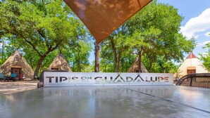 A sign with "Tips on Guadalupe" and a concrete area with trees and yurts in the background. - Tipis on the Guadalupe (New Braunfels)