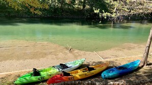 Kayaks lined up on a sandy shore next to a calm body of water. - Tipis on the Guadalupe (New Braunfels)