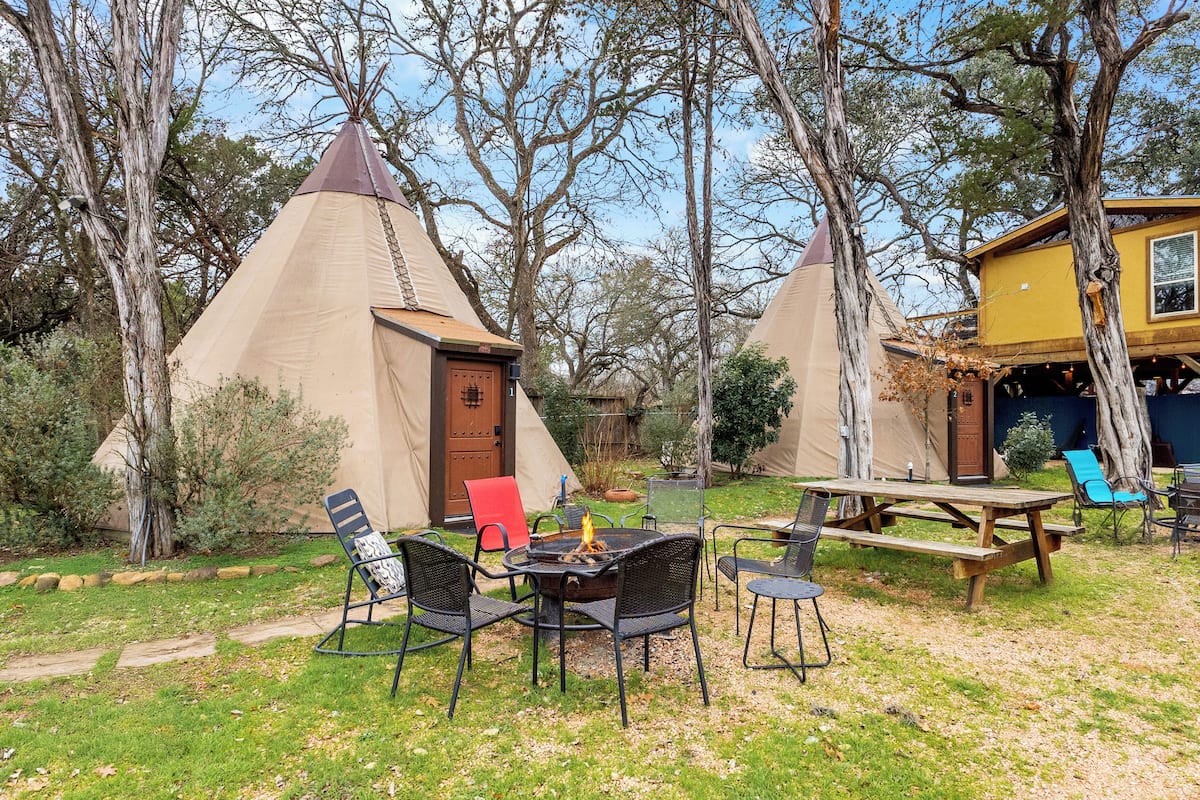 A campsite with teepees, a picnic table, and chairs.