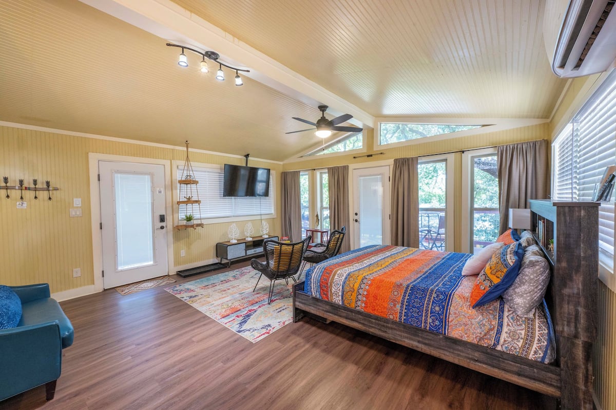 A spacious bedroom with a large bed, a ceiling fan, and a TV mounted on the wall.