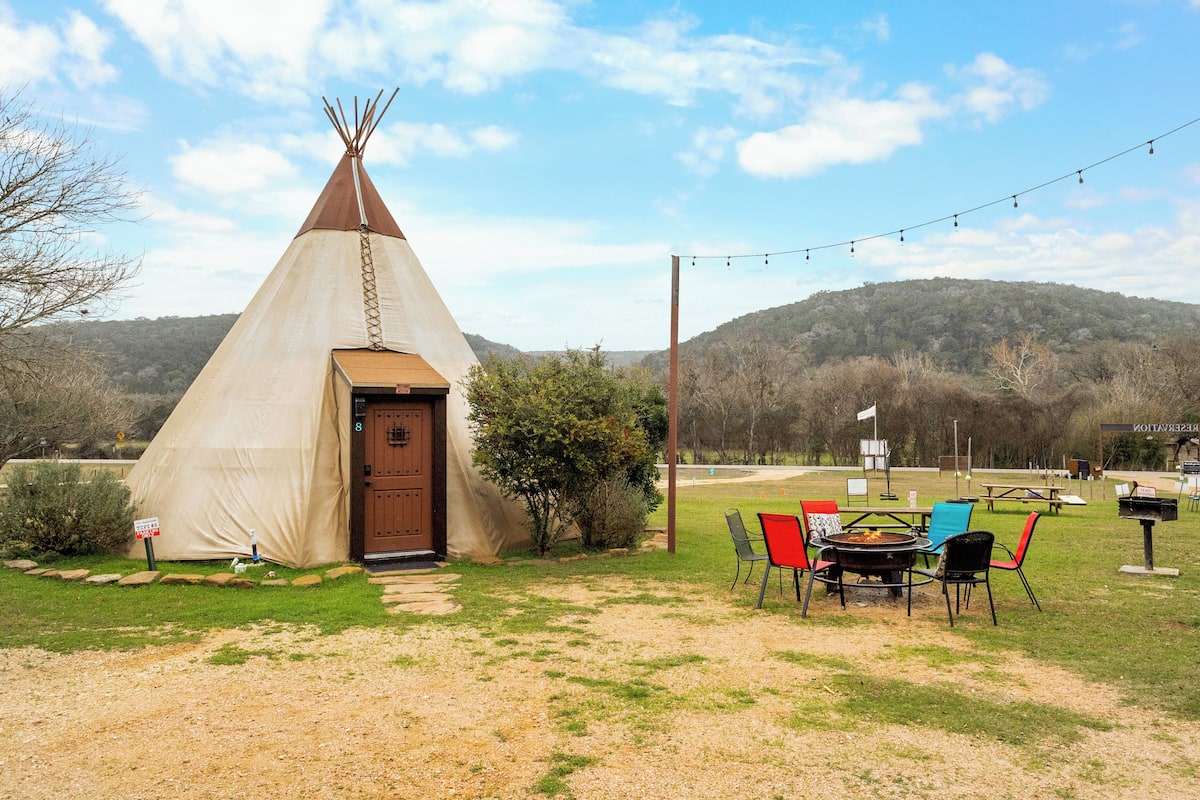 A teepee with a wooden door, a fire pit, and outdoor seating.