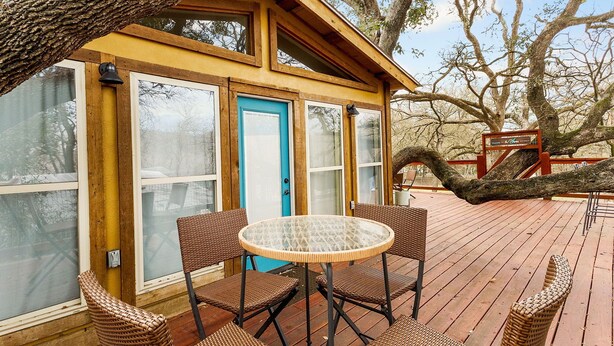 A wooden deck with wicker furniture and a glass table, overlooking a forested area. - Tipis on the Guadalupe (New Braunfels)