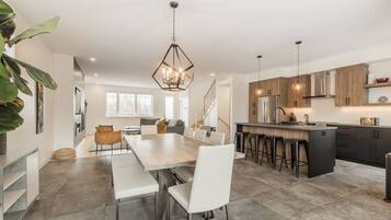 A modern kitchen with a central island, bar stools, and a dining area with a long table and chairs.