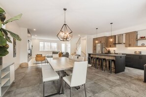 Een moderne keuken met een centraal eiland, barstoelen en een eethoek met een lange tafel en stoelen.