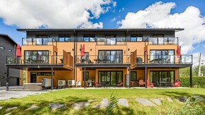 Un immeuble moderne à plusieurs étages, doté de balcons, d’un espace extérieur aménagé pour s’asseoir et d’une pelouse bien entretenue.