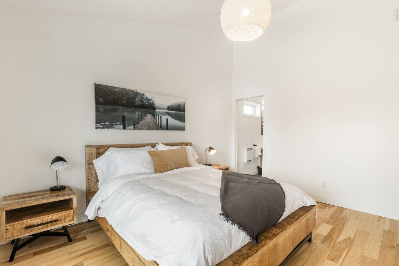 Una camera da letto con un letto in legno, biancheria da letto bianca, un comodino con una lampada e un quadro appeso al muro.