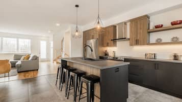 A modern kitchen with a central island, bar stools, wooden cabinets, and pendant lighting.