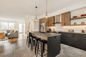 Een moderne keuken met een centraal eiland, barkrukken, houten kastjes en hanglampen.