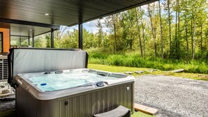 Una vasca idromassaggio esterna con un pontile in legno e un'area coperta, immersa in un paesaggio boscoso.