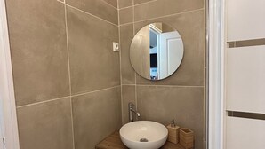 A bathroom with a wooden vanity, a round mirror, and beige tiles.