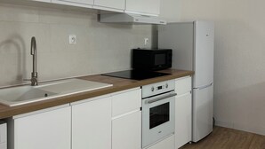 A modern kitchen with white cabinets, a wooden countertop, a sink, a microwave, an oven, and a refrigerator.