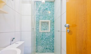 Un baño con cabina de ducha de vidrio, un lavabo blanco y una puerta de madera.