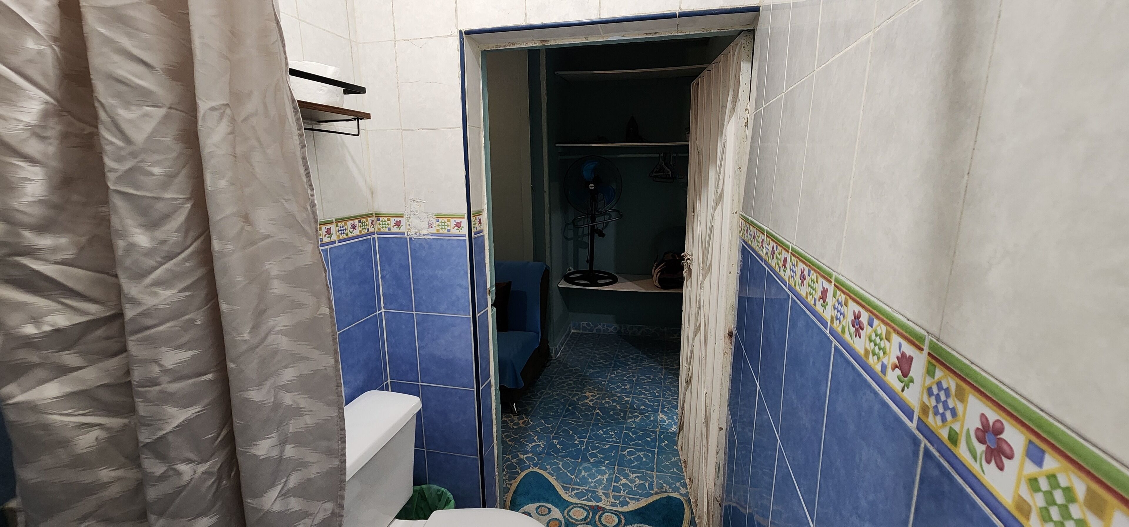 A bathroom with blue and white tiled walls, a toilet, a shower area, and a fan.
