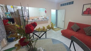Una sala de estar con un sofá rojo, una mesa de comedor con un florero y una cocina con refrigerador y fregadero.