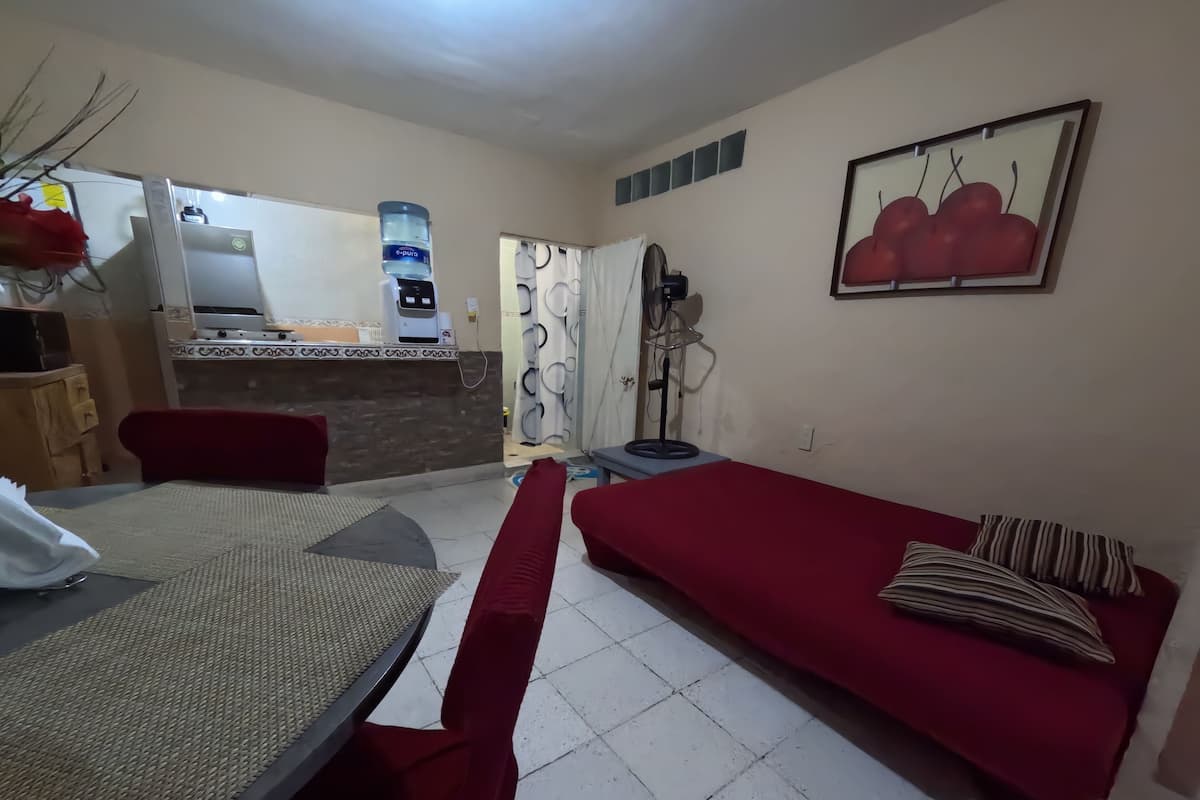A living room with a dining table, red sofa, and a kitchen area in the background.