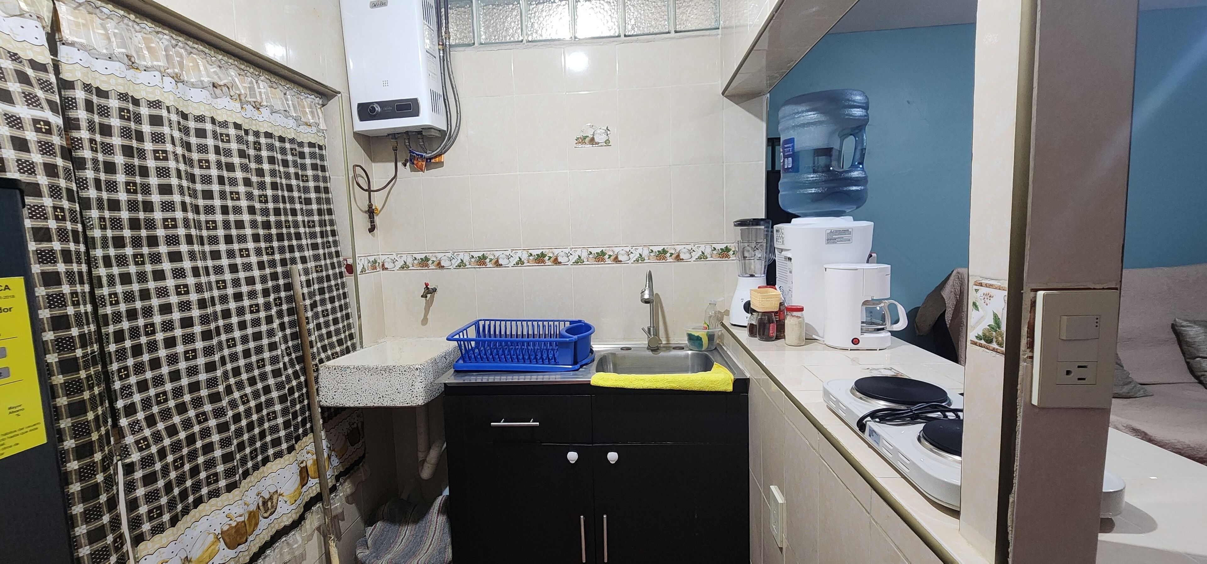 Uma cozinha compacta com pia, uma cesta azul, cafeteira e filtro de água.