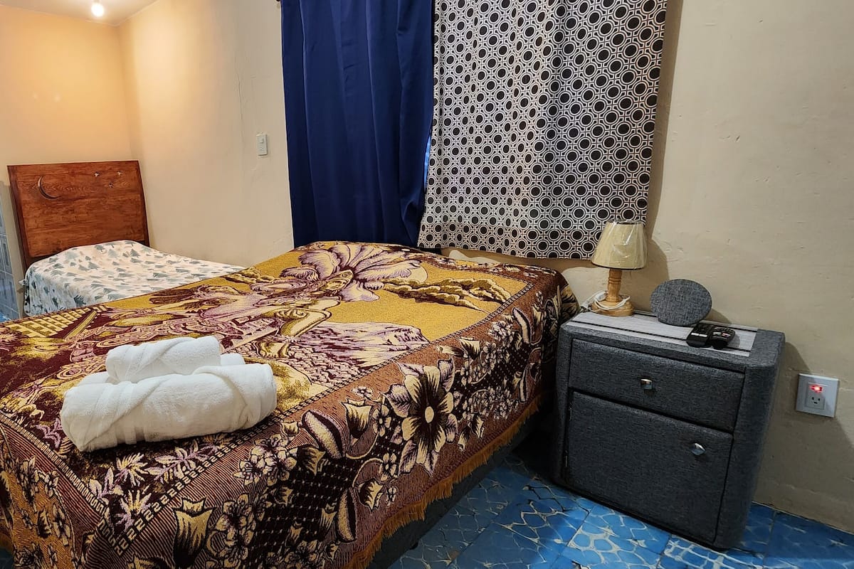 A hotel room with a bed, a nightstand, a large water dispenser, a wardrobe, and a patterned curtain.
