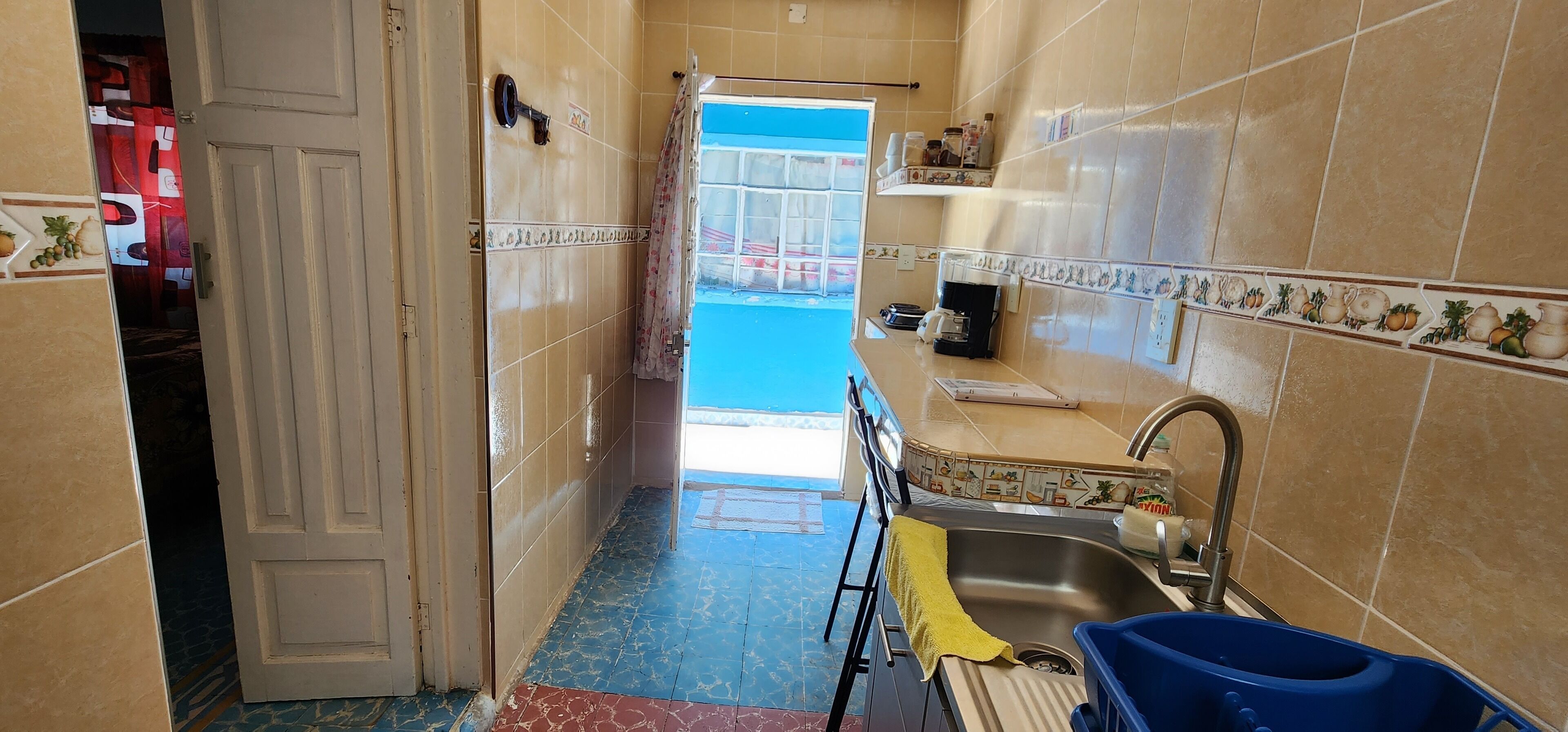 A narrow kitchen with a sink, a window, and a door leading to another room.