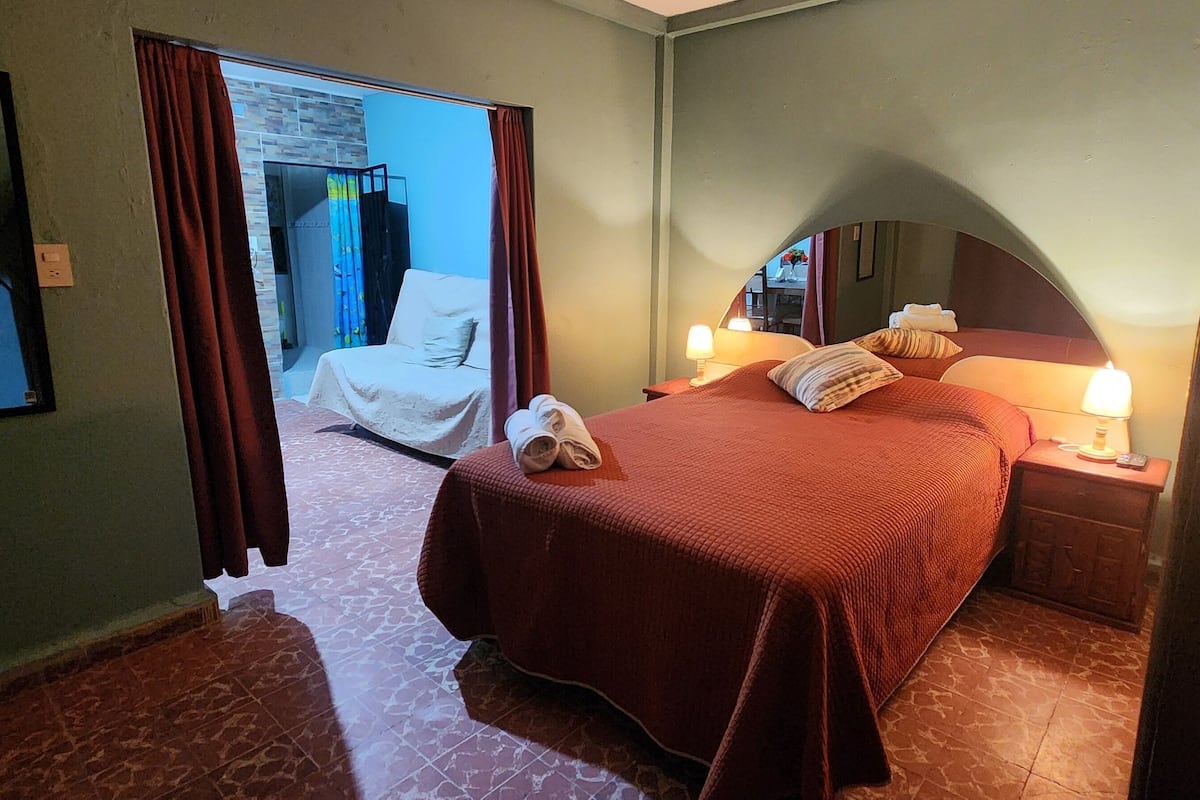 A hotel room with a bed, a chair, a nightstand, and a mirror.