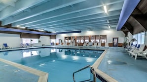 Une piscine intérieure à l’eau d’un bleu cristallin, entourée de chaises longues et d’une terrasse en bois.