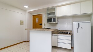 Une cuisine compacte avec des meubles blancs, un four à micro-ondes, une cuisinière à gaz et un réfrigérateur blanc.
